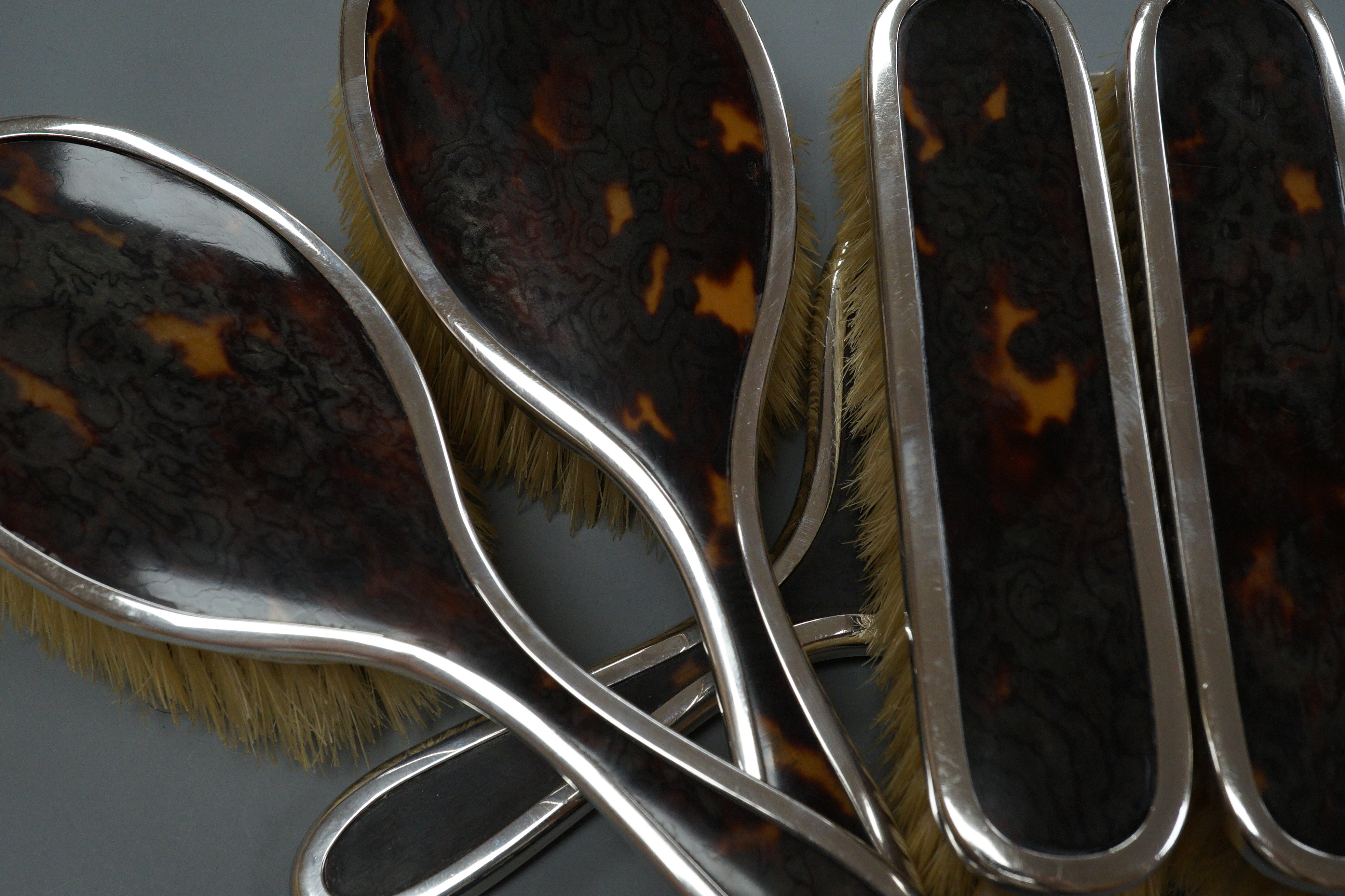 A George V matched silver and tortoiseshell mounted five piece mirror and brush set, a George V silver and tortoiseshell pique mounted circular box with mirrored interior and a similar mounted glass toilet jar.